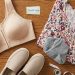 Flatlay of inclusive fashion essentials featuring a front-opening supportive bra, wide-fit comfort shoes, and a floral plus size blouse.